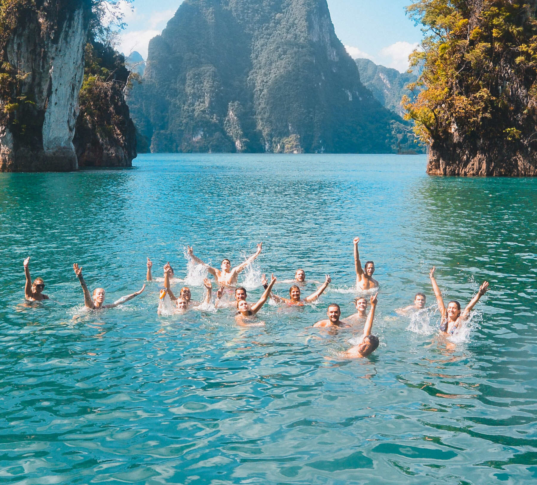 Groep jongeren zwemt en juicht in het turquoise water van Khao Sok Lake, omringd door kalksteenrotsen